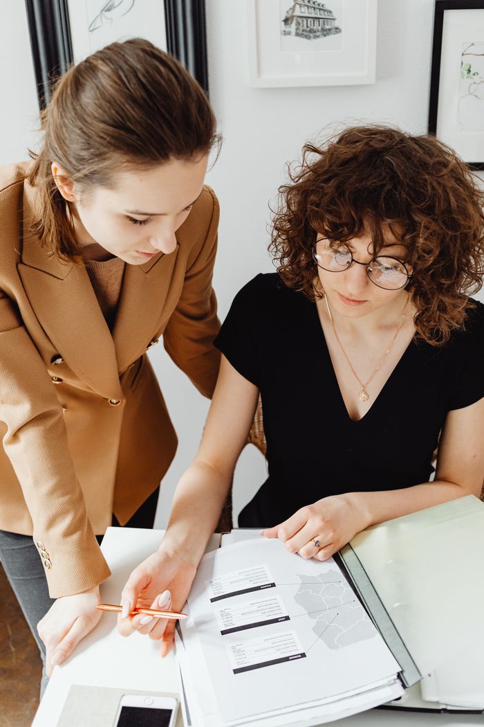 Two businesswomen working together, analyzing documents, and discussing ideas at an office desk.